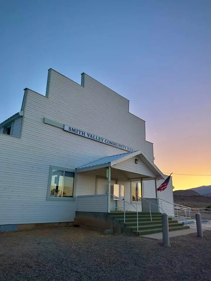 Smith Valley Community Hall at sunset, white siding and stepped front, flag by the steps.